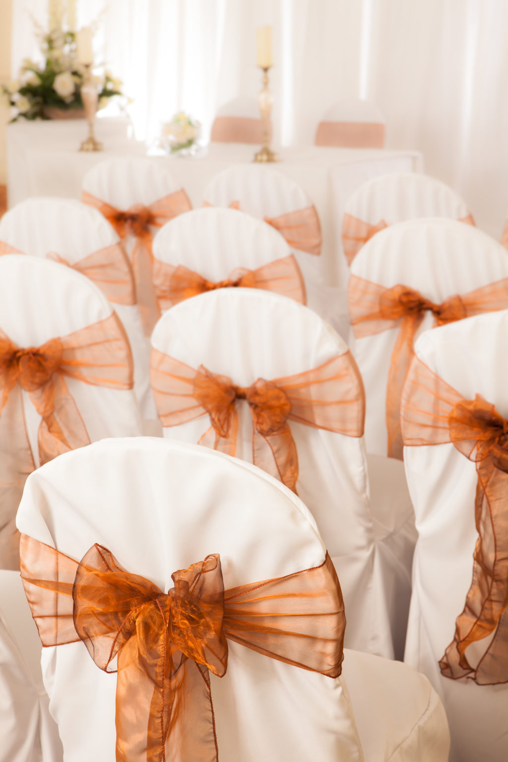 White wedding bouquet in the background with chairs in foreground arranged in rows and dressed with ribbons